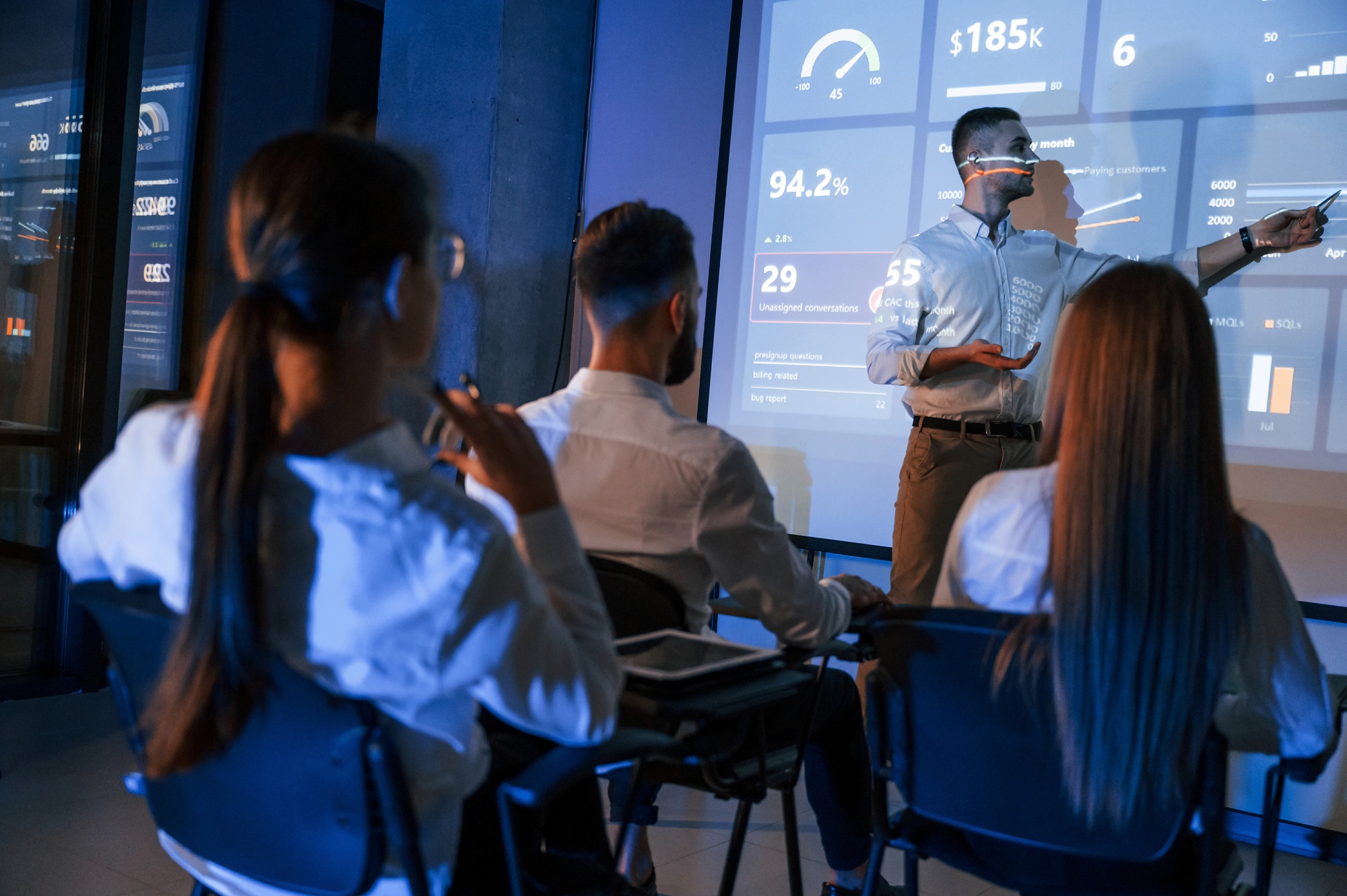 Male leader talking to employees, the projector in office of stock exchange company
