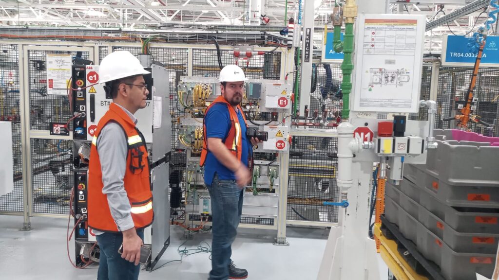 Equipo de producción de video corporativo industrial grabando en planta de manufactura con personal y maquinaria en operación.